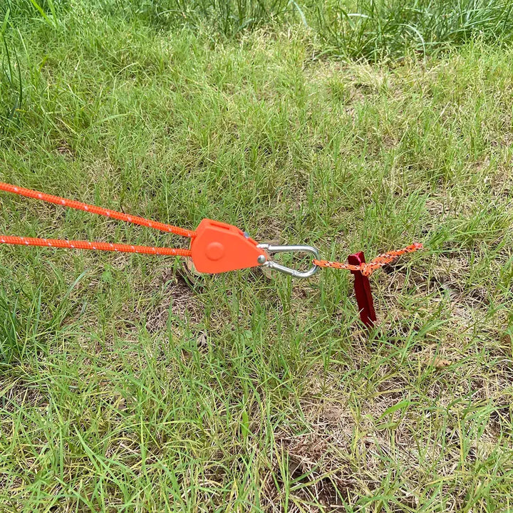 Orange camping rope pulley tensioner secured in grass with red stake