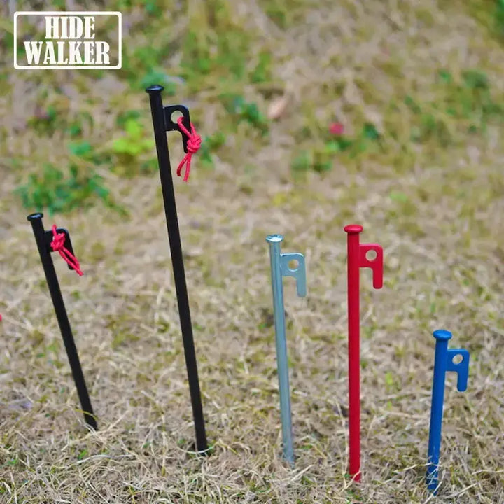 Various colored steel tent pegs and ground nails on grass, ideal for outdoor camping canopies and flysheet tarp accessories.