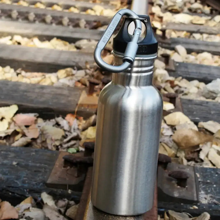 Stainless steel water bottle with carabiner attached, displayed outdoors on a railway track.