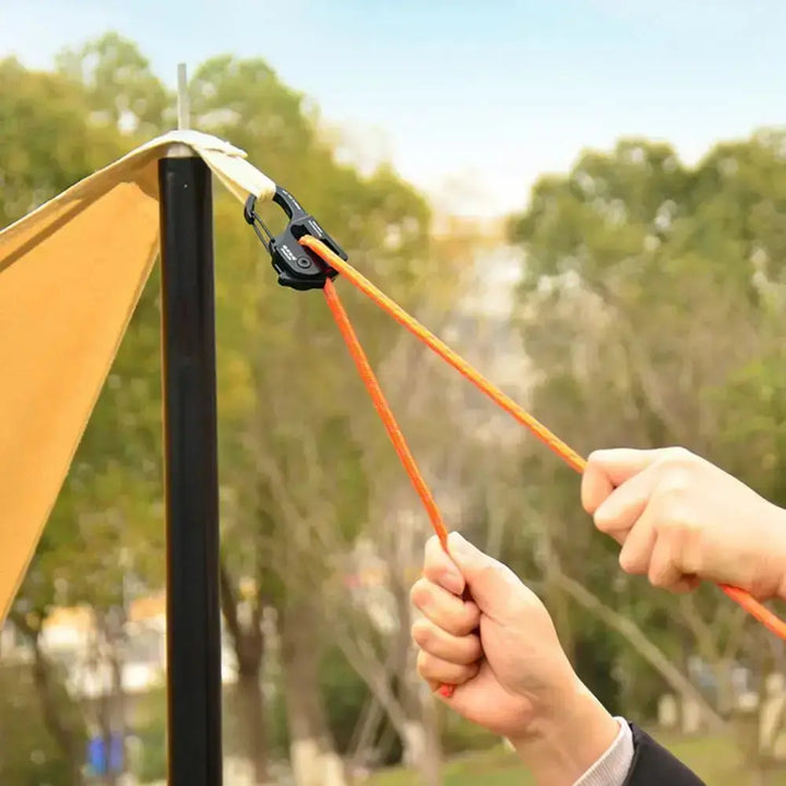 Aluminum alloy tent rope tensioner adjusting an orange cord on a camping setup outdoors.