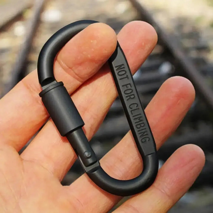 Hand holding a black D-shape carabiner with "Not for Climbing" text, suitable for fishing and camping.