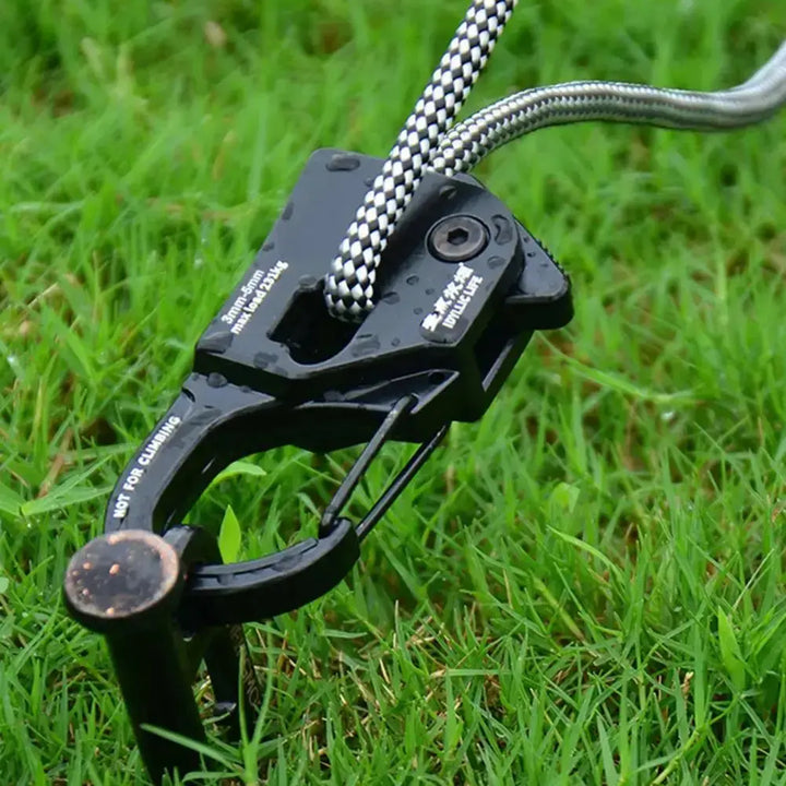 Mini aluminum rope tensioner on grass for camping tents, adjustable cord fastener, rustproof and lightweight design.